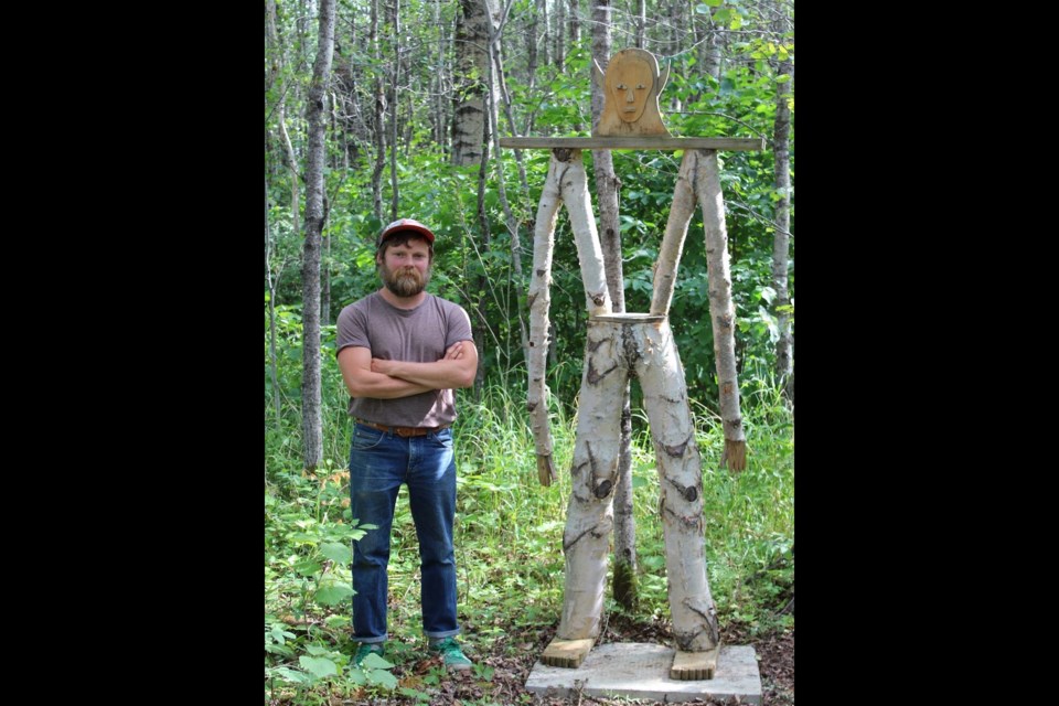 A walk in the woods south of Colinton July 11 provided an opportunity for more than 25 local art lovers to not only spend some time in nature, but to catch a glimpse of what a few local artists were up to during the COVID-19 pandemic, and long before. The Mossy Trails Boreal Gallery put on its first art walk that Sunday, which included many works by artist Nickelas “Smokey” Johnson, pictured with his piece 
Unnamed God (Birch).” Johnson is also the artist behind the “Ripped off and Red” sculpture of a giant, disembodied
hand that was moved from its long-time home in Edmonton to his parents’ property at Mossy
Trails late last year. 