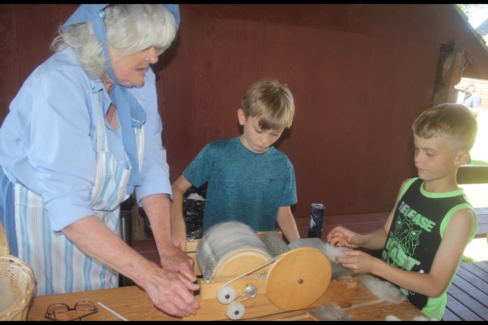 Sue Huberdeaux instructs Fort Assiniboine students Hendrix Schuurman and Wendel Wood in how to pull wool out of a device used for carding on June 6.