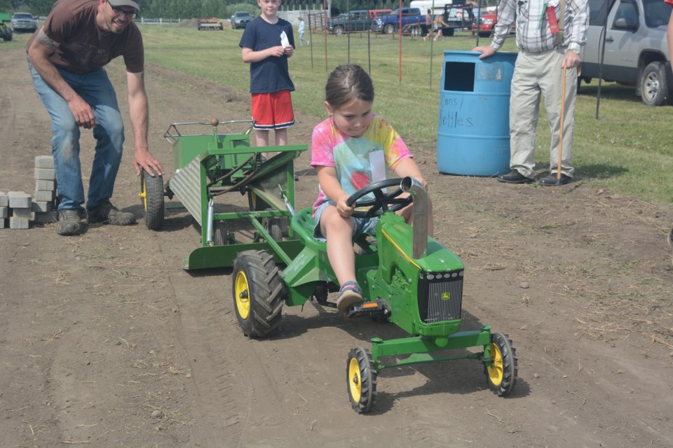 Natalie Taylor gets a bit of assistance from club president JD Woynorowski in the kids pedal tractor pulls during the first day of the event, June 3. 