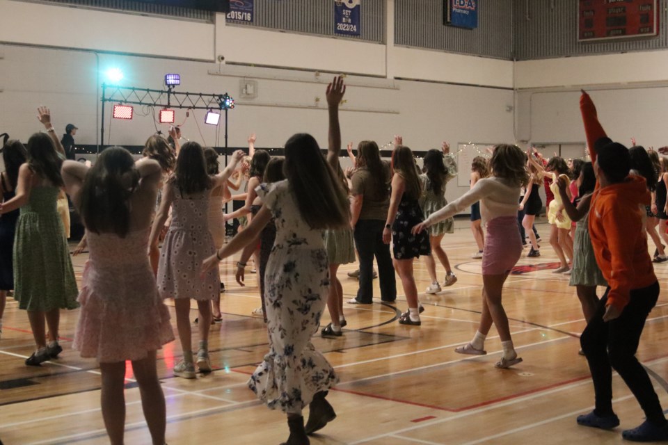 A large group of students follows the Just Dance steps on the screen above. 