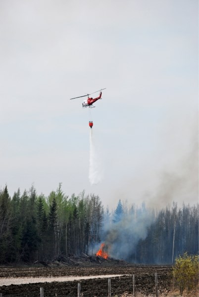 A helicopter drops water on a fire near the Al-Pac millsite Sunday