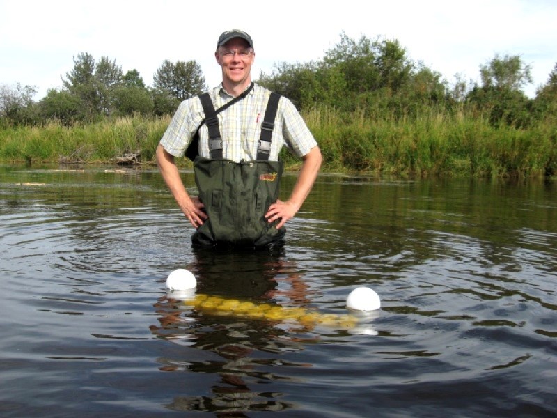 Lawton Shaw, assistant professor of chemistry at Athabasca University, stands in the Battle River with a chemical diffusing substrate, an apparatus used to test the effects