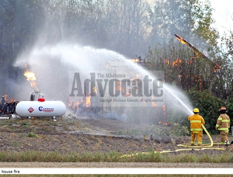 A firefighter from Athabasca stays a safe distance away as he uses water to cool down a large propane tank at a fire on a property along Paxson Road and Range Road 203 last
