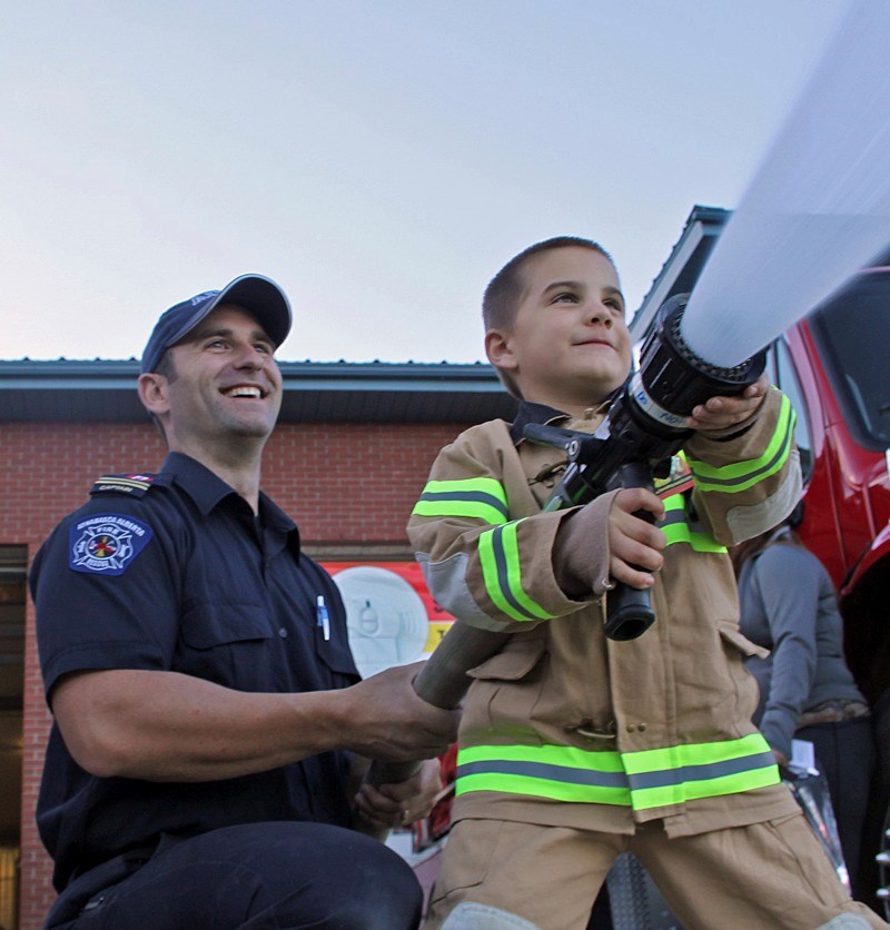 Athabasca Fire Department captain Bryan Hall provides backup support for young Cody Gauthier while he takes a turn on the nozzle of a hose during the department&#8217;s open