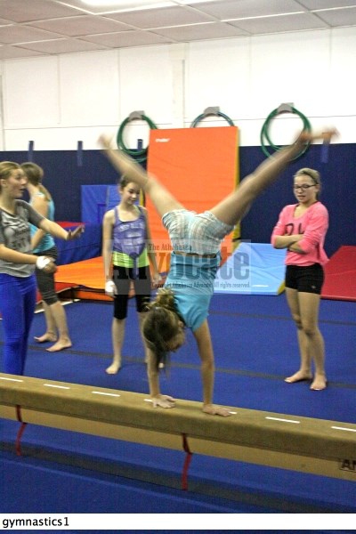 Hannah Maton performs a cartwheel on the training balance beam in front of some other gymnasts.