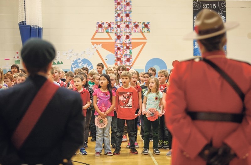 Athabasca Legion president Jacqueline Jonk (left) and RCMP Const. Sandy DesJardin stand and listen to Whispering Hills Primary School students sing during their Remembrance
