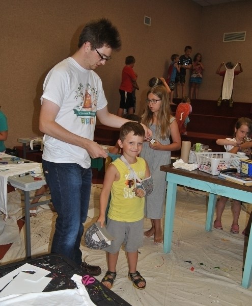 Scott Franchuk (l), shown here helping Cole Bentz put on the cape for a superhero during the Barrhead Public Library &#8216;s Summer Reading Club program, will head the