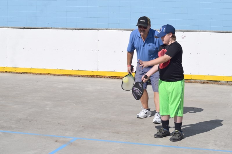 Dennis Lafleur (back) gives some pointers to nine-year old Ryder Hosack on how to serve.