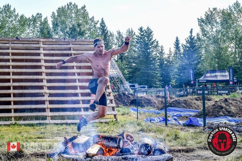 Murray Tuininga jumping over a burning fire on his way to the finish line in a Spartan Race in Red Deer.