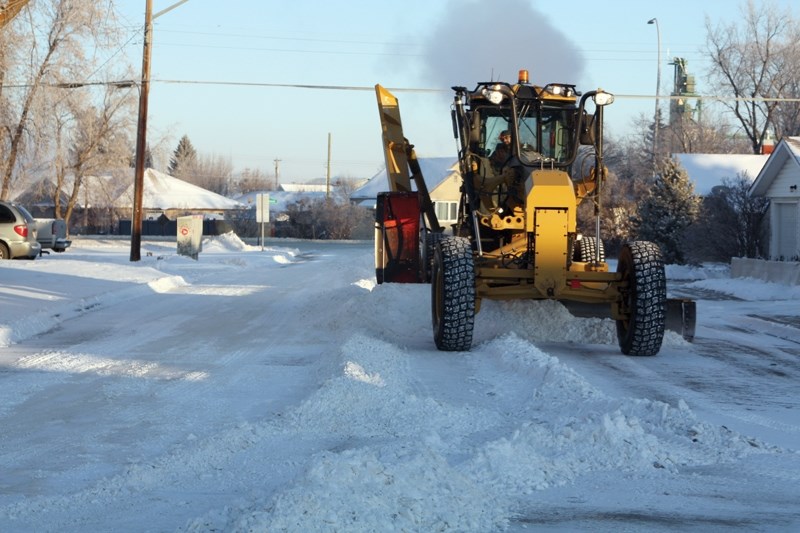 The town’s lone grader clears the snow off a road in town. Residents are asked to move their vehicles off roads where posted and to keep their sidewalks clear.