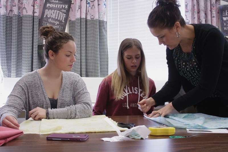 R.F. Staples Fashion and Textiles teacher Keltey Buchko assists students Reese Olsen and Tyra Warwaryk with their pillowcase dresses. The school is hoping to send at least 75 