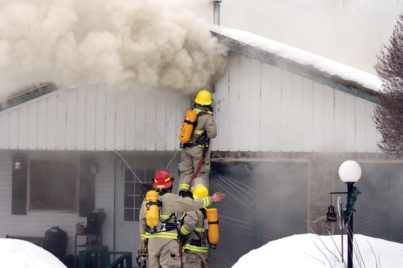 Smoke billows out of the windows of the house while county firefighters work to put out the flames on Saturday.