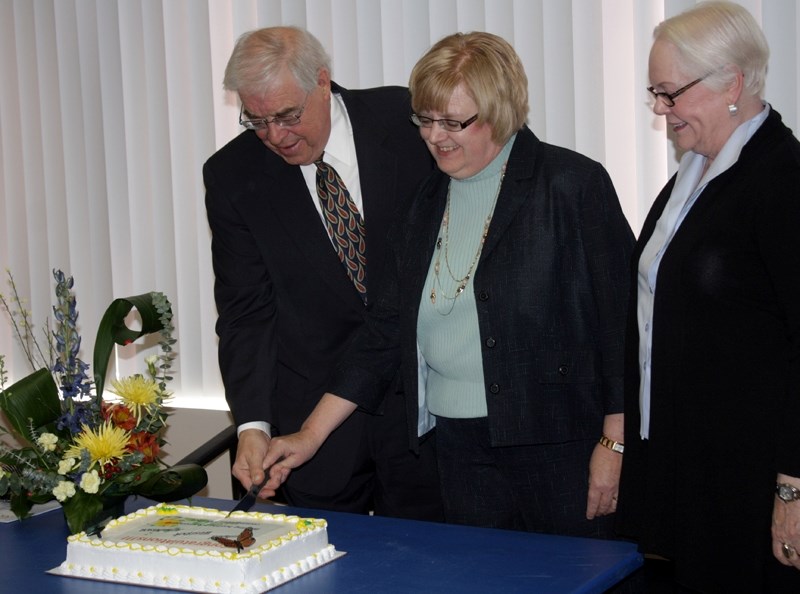 MLA Ken Kowalski cuts a cake with Healthy Families Healthy Futures executive director Linda West (centre) and board chair Shirley Morie celebrating the $1.1 million funding