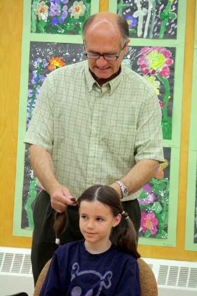 Teacher Rick Mueller starts to cut two pigtails off 12-year-old Codie Belanger&#8217;s head at Busby School May 26. Codie had 14 inches of his hair cut off to donate to be