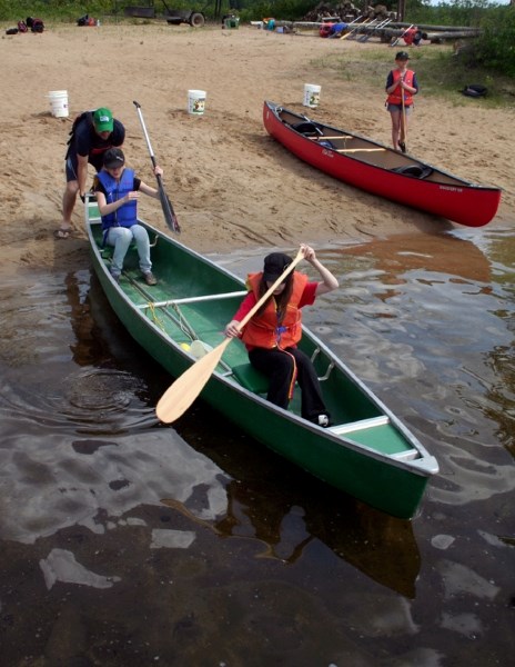 Teacher Robert Weiss gives a helpful push to students Shay Taberner and Breanne Hunt, who were having trouble launching their canoe from the shore of Long Island Lake last