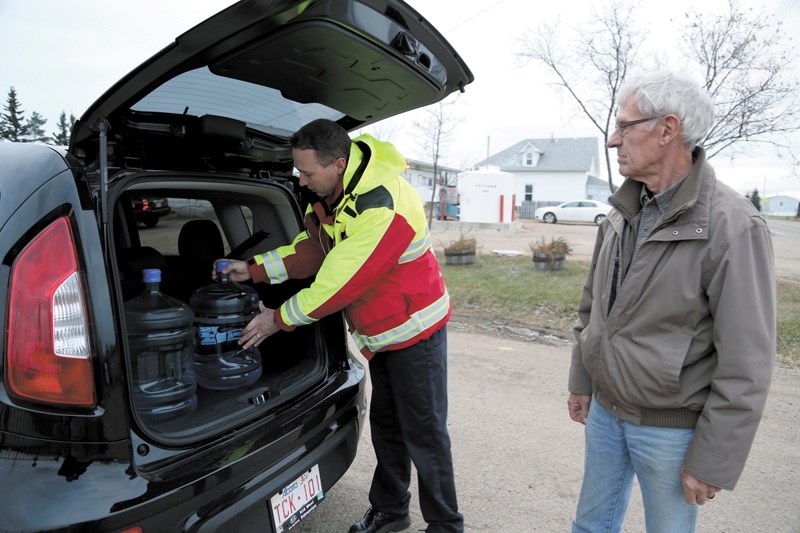 Busby fire chief Jered Stitsen helps load bottles of water into Jim Sterling&#8217;s vehicle during the afternoon water pickup Friday. Fresh bottled water will be available