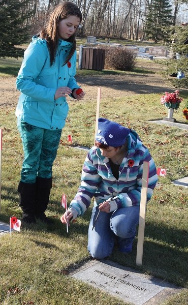 Students from St. Mary School, R.F. Staples School and Rochester School laid flags and poppies at the graves of veterans on Friday. Sydney Kuhberg and Katya Kostiw affix a