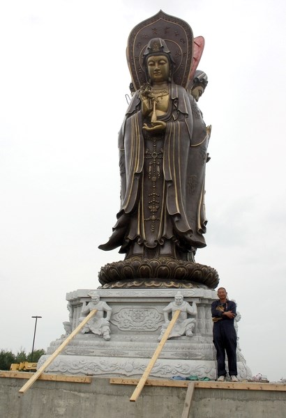 Khai Tran, a volunteer at the Westlock Meditation Centre, with a 10-metre statue of Avalokitesvera, a bodhisattva. The statue is part of an impressive meditation garden set