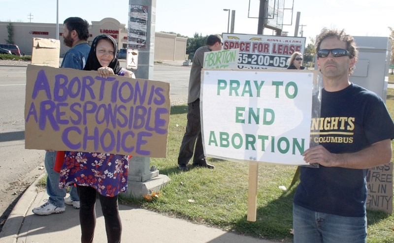 Jennye Blain (left) and Claude Seguin (right) hold up signs with contrasting messages during a demonstration at the junction between highways 18 and 44 on Sunday. About 50 to 