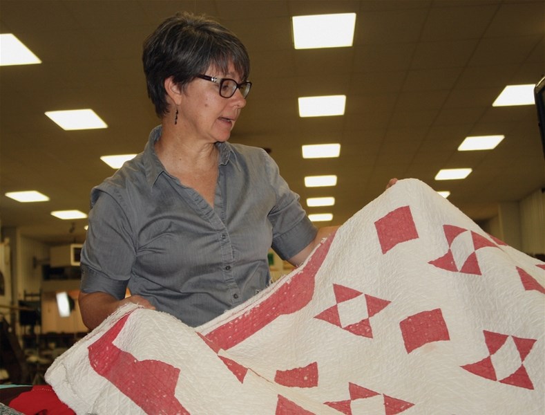 Royal Alberta Museum curator of Western Canadian history Lucie Heins examines a century-old wedding quilt brought in by Elaine Carol-Lawton at the Pioneer Museum on July 16.