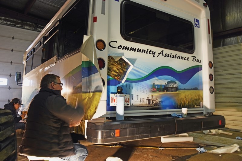 Wayne (front) and Ryan Hackie place decals on the bus from inside the town’s old recycling shop Feb. 10. The new Community Assistance Bus arrived on the Town of Westlock’s