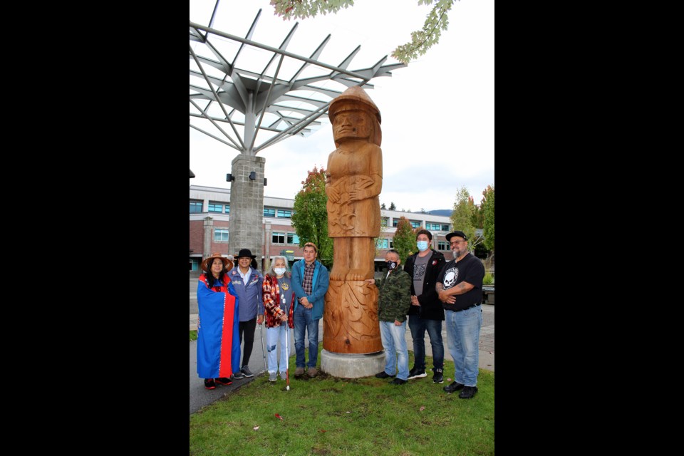 A group photo around the new Welcome figure includes KFN Elders, Chief Ed Hall, councillors George Chaffee and John Peters, and carver Gerry Sheena.