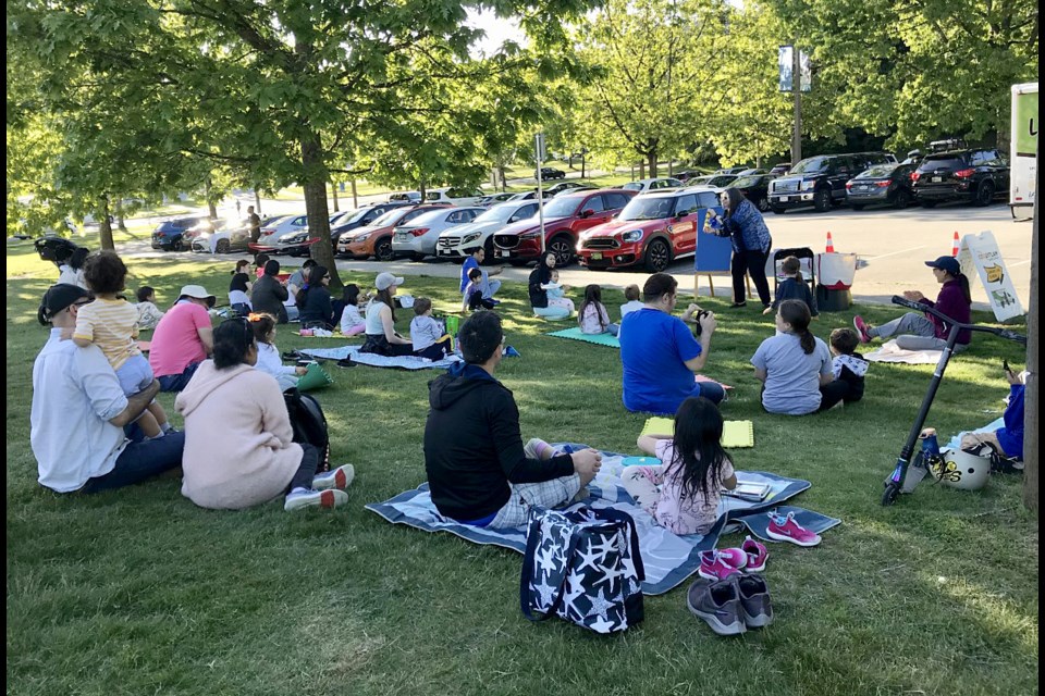 A program assistant with the Coquitlam Public Library reads a story to families at Town Centre Park in Coquitlam during a Library Link visit to the neighbourhood.