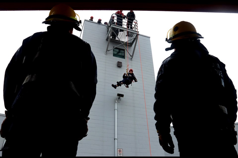 Firefighters from Coquitlam Fire Rescue watch as students in the junior firefighter academy descend from the training tower.