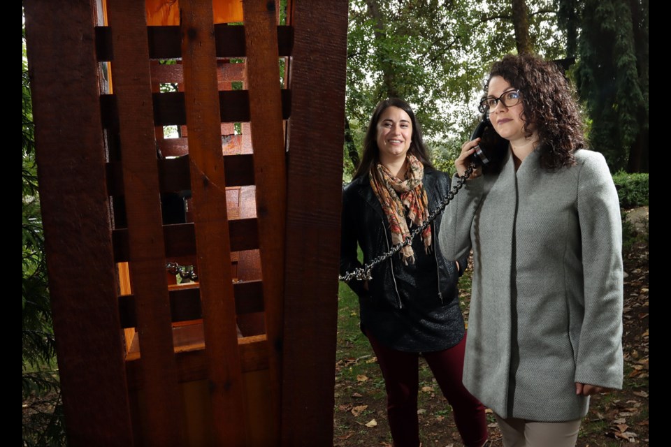 Amelie Lambert and Brittany Borean, of Crossroads Hospice, place a call from the new phone of the wind that's been installed in Port Moody's Pioneer Park to allow grieving family members to place a "call" to their departed loved ones.