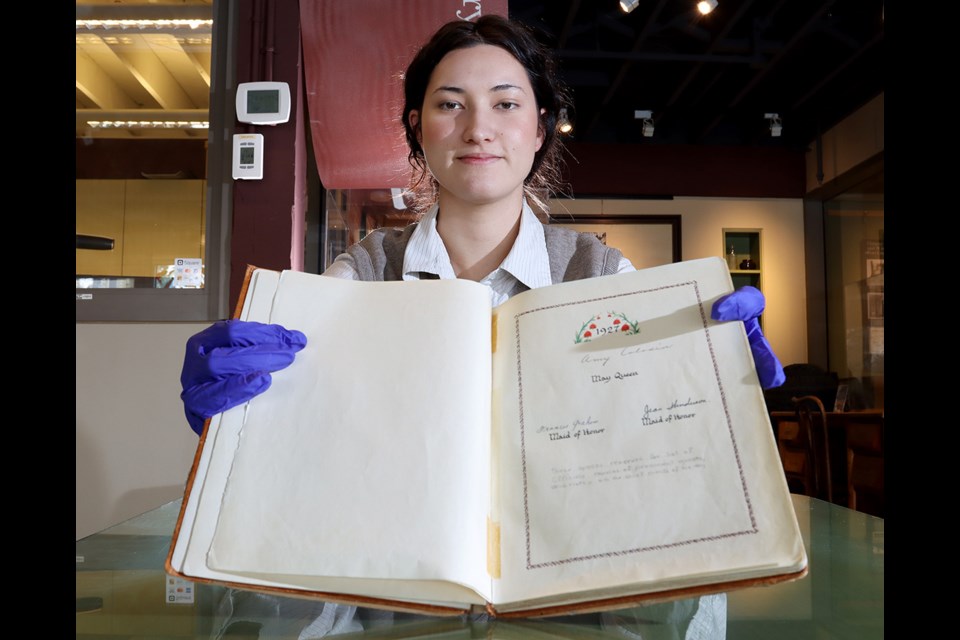 Cynthia MacMillan, an intern at PoCo Heritage Museum and Archives, displays a May Queen registry book that covers all the May Day suites from 1925 to 1975.