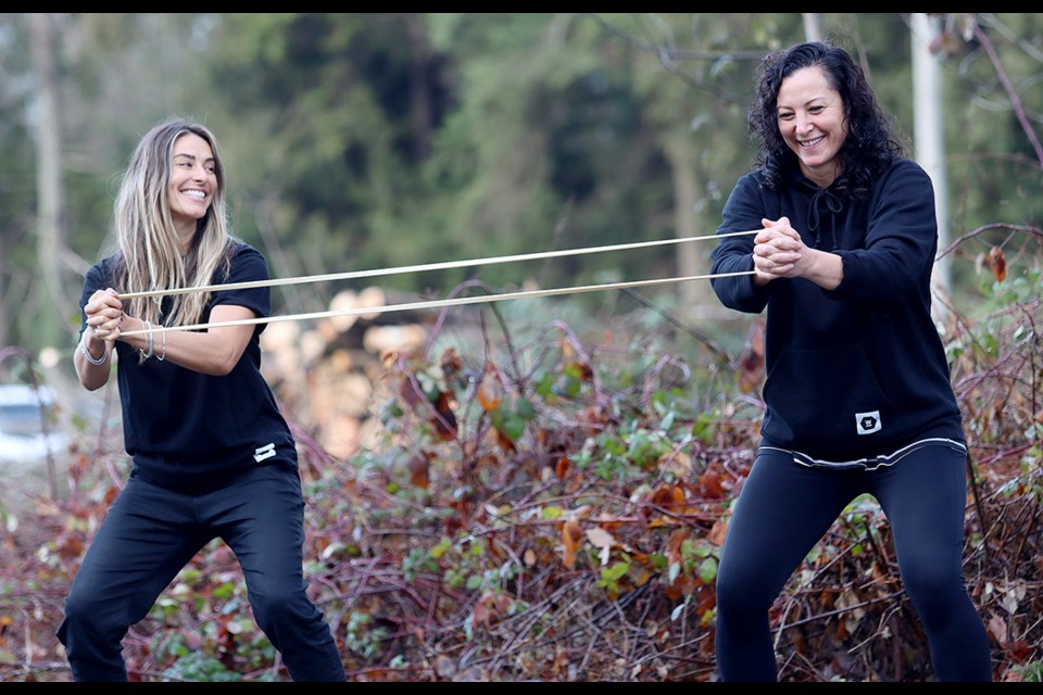 Former Canadian national soccer teammates Melissa Tancredi (right) and Selenia Iacchelli work the exercise band across the street from their new performance clinic in Port Moody, where construction is underway to transform Inlet Field into a FIFA-regulation field turf facility.