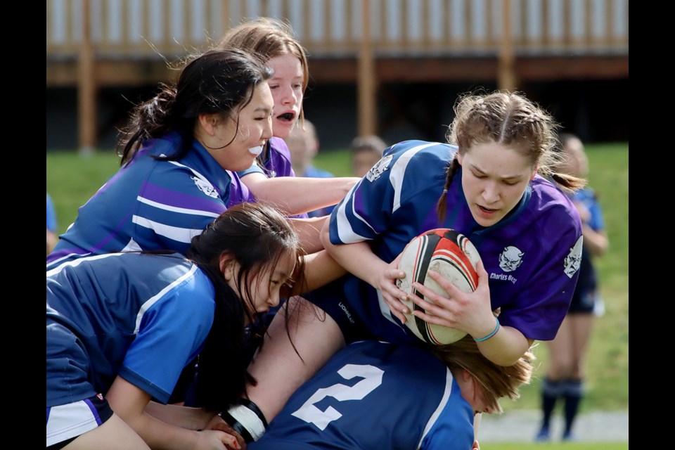 Jorja Erven-Cook, of the Dr. Charles Best Blue Devils is swarmed by Port Moody Blues tacklers at Thursday's girls' high school rugby jamboree at École Banting Middle School in Coquitlam.