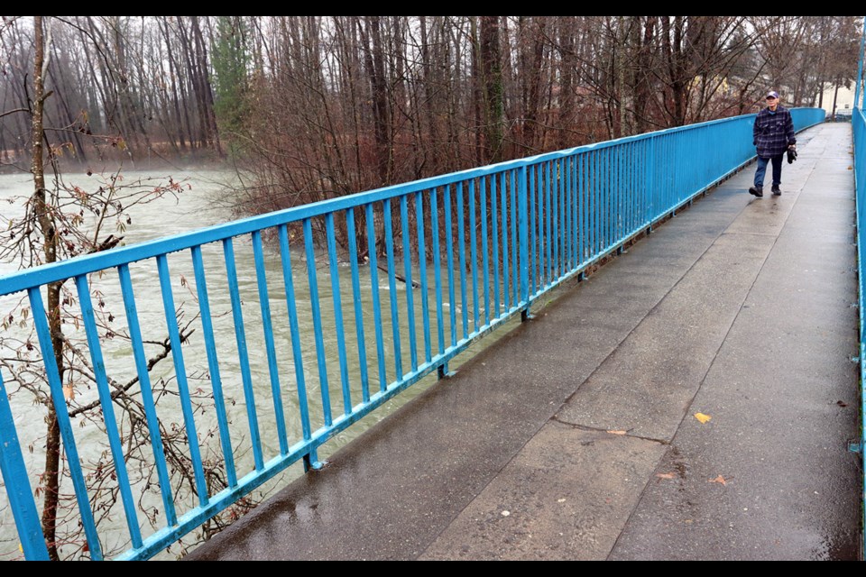 MARIO BARTEL/THE TRI-CITY NEWS
A pedestrian traverses the McAllister foot bridge over the swollen Coquiitlam River on Monday. After a brief pause more heavy rain is expected on Tuesday.