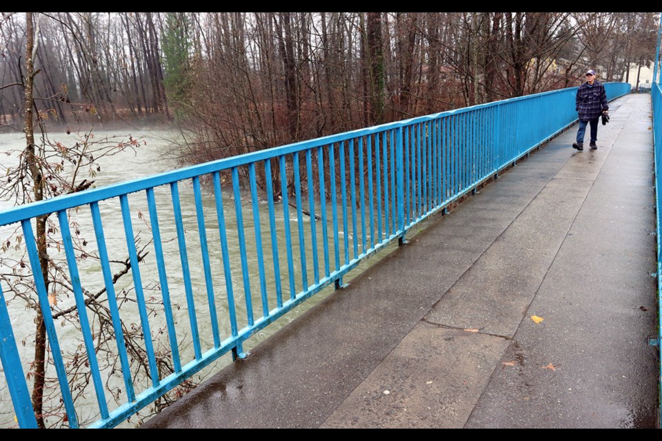 MARIO BARTEL/THE TRI-CITY NEWS
A pedestrian traverses the McAllister foot bridge over the swollen Coquiitlam River on Monday. After a brief pause more heavy rain is expected on Tuesday.