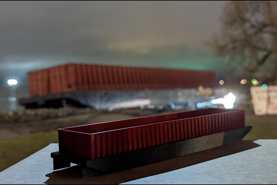 The mini 3D printed English Bay Barge stands in the foreground of its inspiration. 