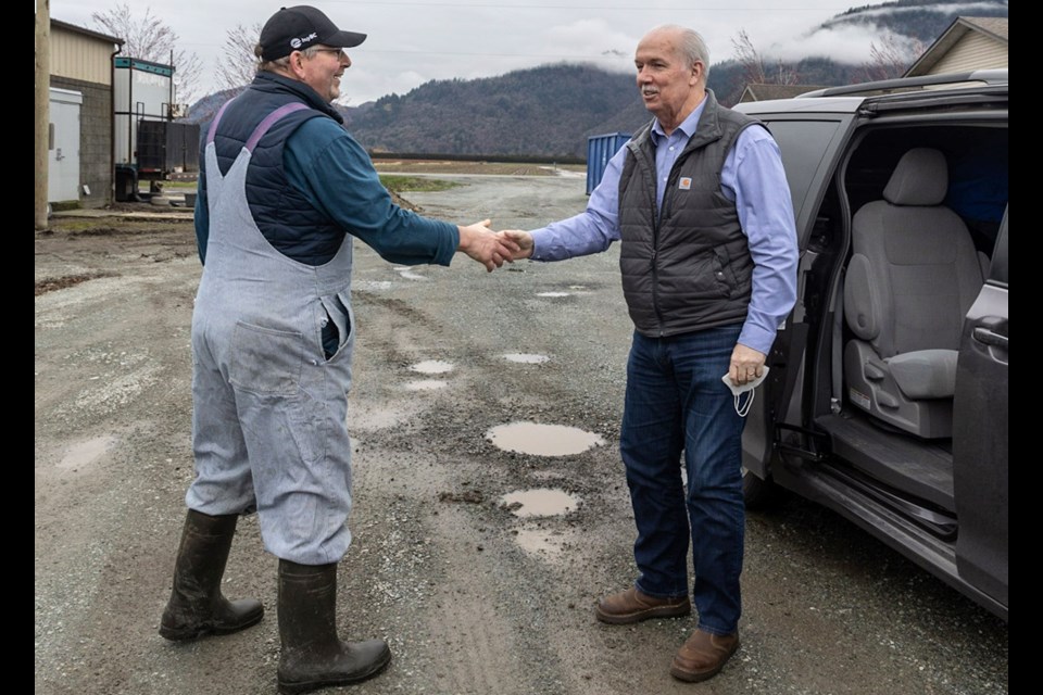 Premier John Horgan shakes the hand of a man on a farm in the Fraser Valley