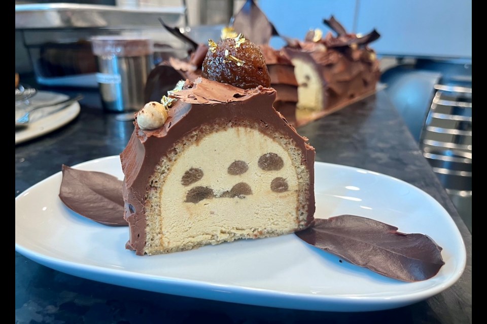 A slice of Chestnut Buche de Noel shows the rich chocolate ganache-coated hazelnut sponge cake with chestnut cream and candied chestnuts inside