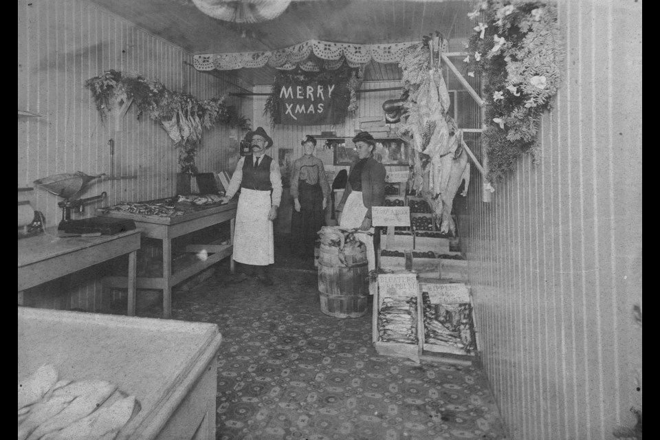 A trio stands in a fish shop decorated for Christmas in 1904. CVA 1133-08 