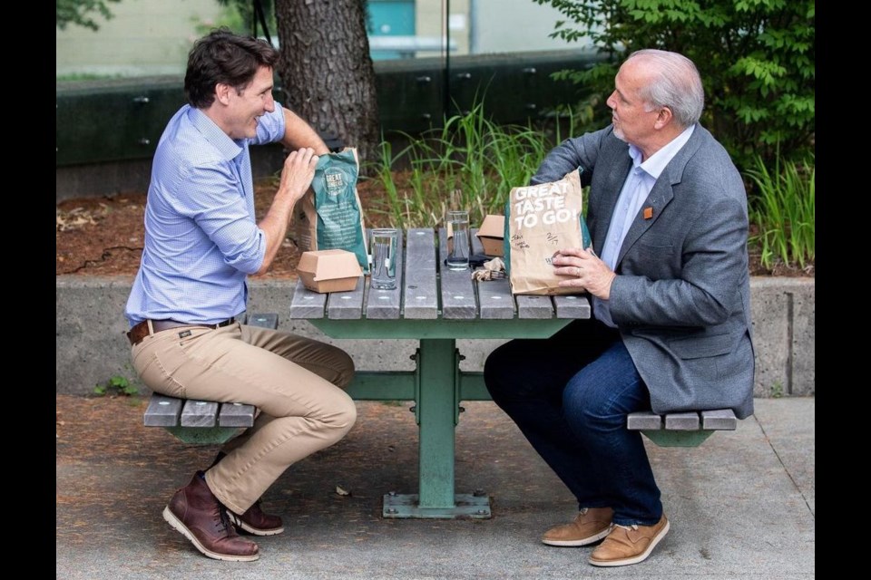 Prime Minister Justin Trudeau, left, and B.C. Premier John Horgan sit down at a picnic table with take-out food from the White Spot in Coquitlam.