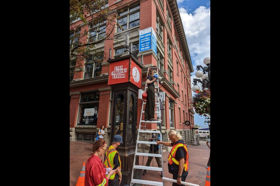 A protester stands on a ladder with a megaphone beside the Gastown Steam Clock. 