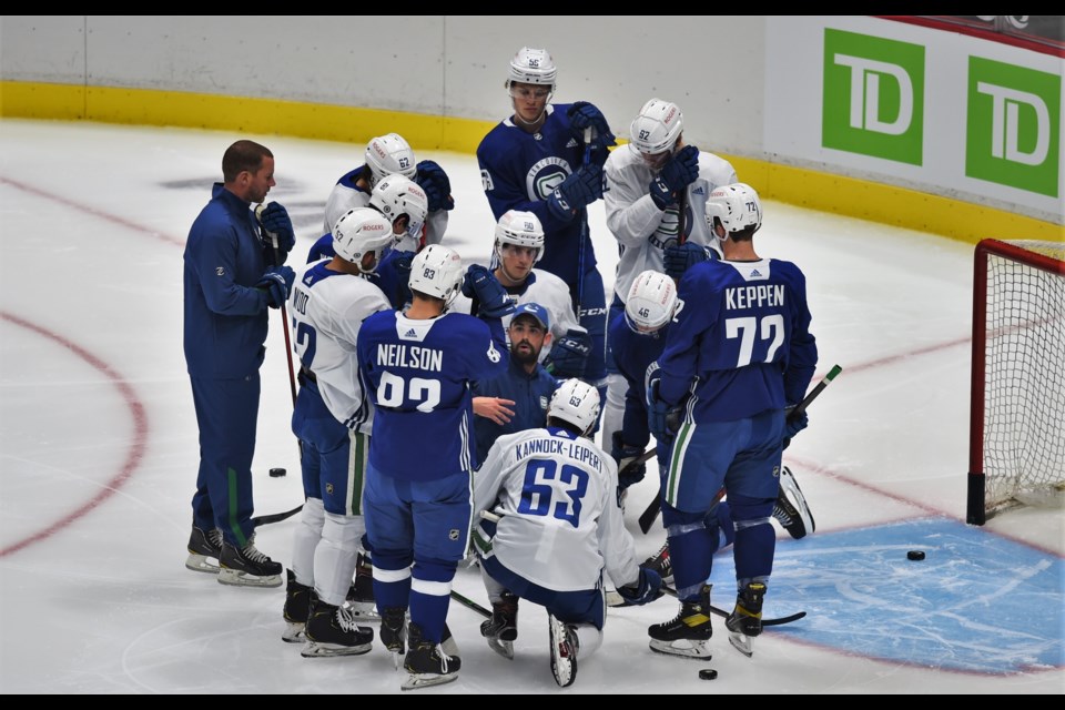 Canucks skating coach Mackenzie Braid explains concepts to a group of Canucks rookies, including Vasily Podkolzin, Danila Klimovich, Viktor Persson, Jett Woo, Tristan Nielsen, Alex Kannok Leipert, and Ethan Keppen, as Abbotsford Canucks GM Ryan Johnson looks on.