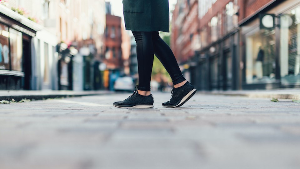 Close-up, low section of young woman wearing sneakers, walking down urban street.