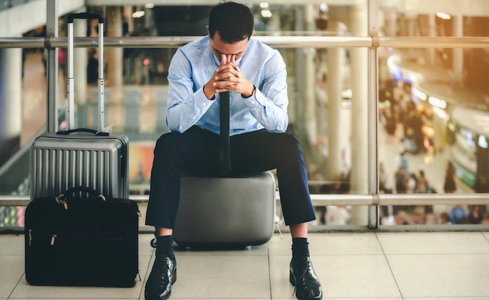 man-sitting-on-luggage-airport-distressed