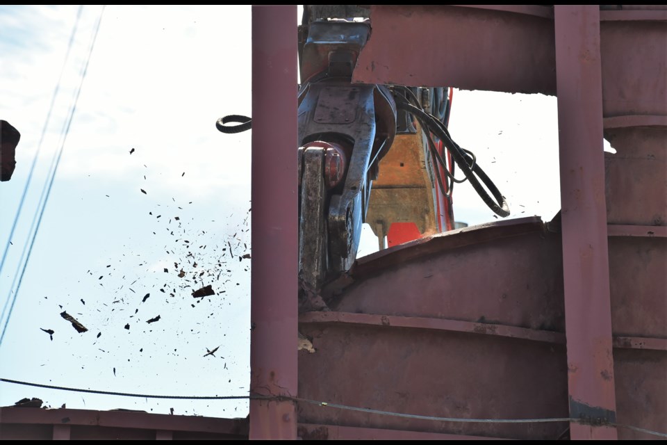 Debris flies as an excavator with specialized cutting jaws rip pieces of the English Bay Barge off.