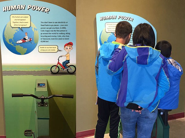  A family reading up on sustainability in the museum’s Kids Gallery. The bike on the left interactively shows how human power can generate energy.