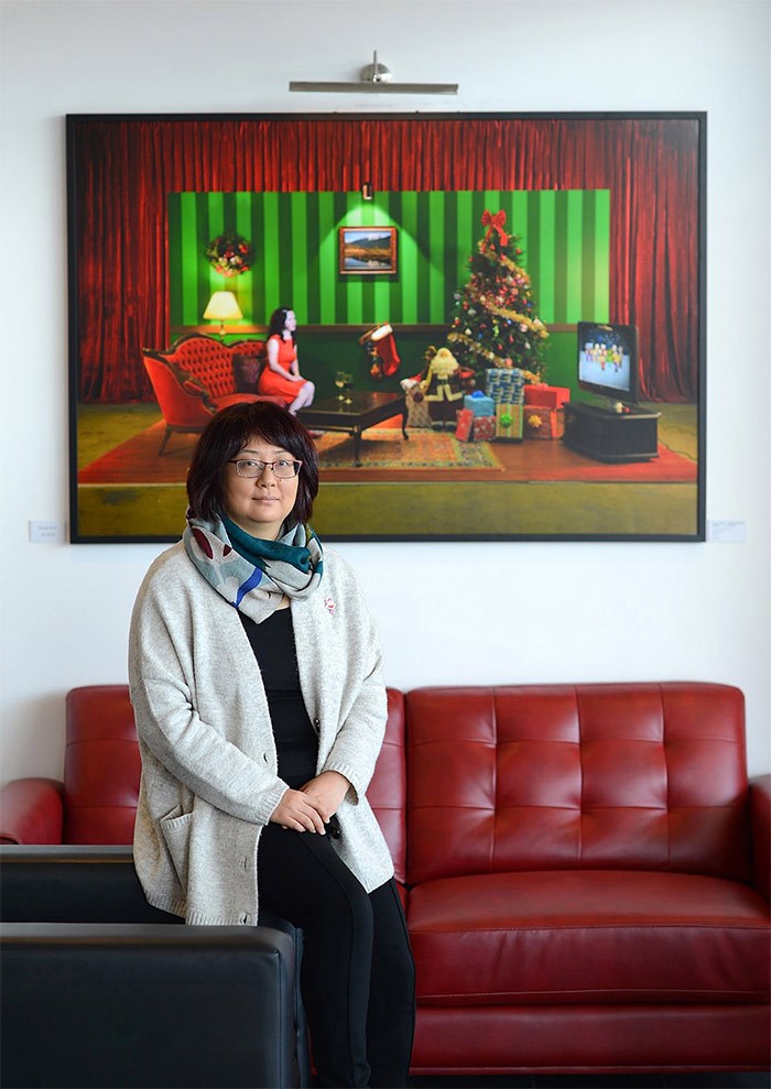  McAfee is pictured in front of a conceptual photo of Richmond artist Fang Tong, in which a female immigrant is celebrating Christmas at home alone. Photo by Boaz Joseph News/Special to the News
