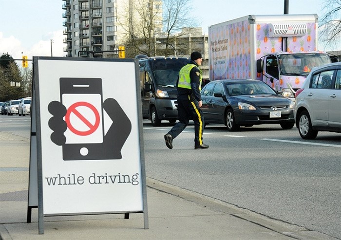  A North Vancouver RCMP officer prepares to issue a ticket during a distracted driving enforcement blitz in March 2018. A woman issued a three-month driving ban after she picked up her phone to dial 911 at a red light has had the ban overturned in court. photo Cindy Goodman, North Shore News