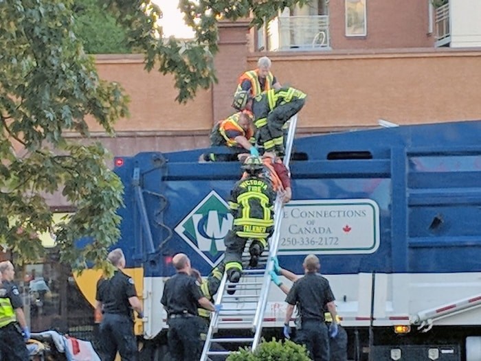  A man is lifted from the trash-compacting box of a garbage truck operating near the intersection of Johnson and Vancouver Streets on Wednesday, Aug. 1, 2018. (Photograph By ALBERT RIOPEL)