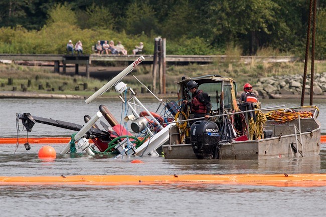  Workers watch as a capsized tugboat is lifted from the Fraser river between Vancouver and Richmond, B.C., on Wednesday, August 15, 2018. THE CANADIAN PRESS/Ben Nelms