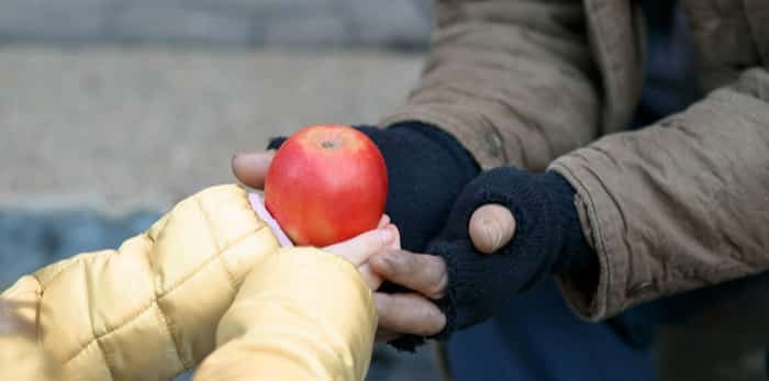  Kind little child gives apple to a homeless person / Shutterstock